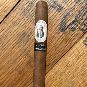 Brown cigar with Black Patch Cigar Co. band and a '20th Anniversary' label on a wooden surface.